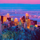 City skyline at dusk with illuminated buildings, river view, snowy hills, purple sky