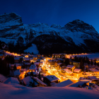 Snow-covered village at twilight nestled by towering mountains under blue sky