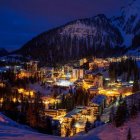 Snowy mountain village at night: warm lights, snow-covered slopes, pine trees