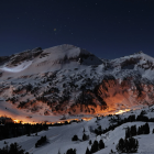 Starry night sky over snow mountains and glowing settlement