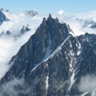 Snow-covered rugged mountain peaks under a blue sky with scattered clouds.