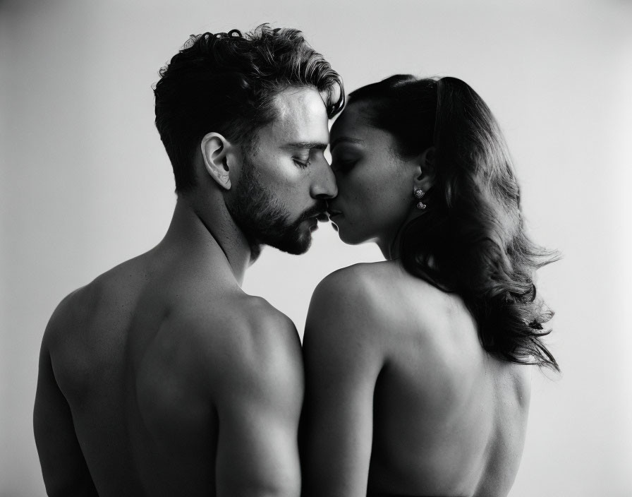 Monochrome image of man and woman in intimate pose against light backdrop