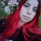 Red-haired person in contemplative pose among pink flowers and greenery