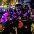 Colorful night scene in a village with people under streetlights & umbrellas