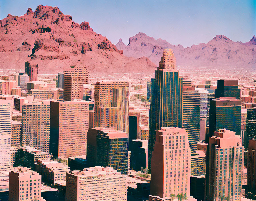 Pink-hued modern city skyline with skyscrapers and mountains in clear sky