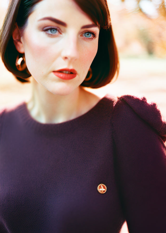 Woman with Short Dark Hair in Plum Sweater and Striking Blue Eyes Gazes at Camera with Autumn