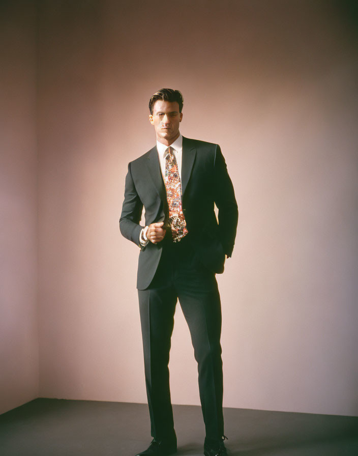 Confident man in dark suit with colorful tie against pink backdrop