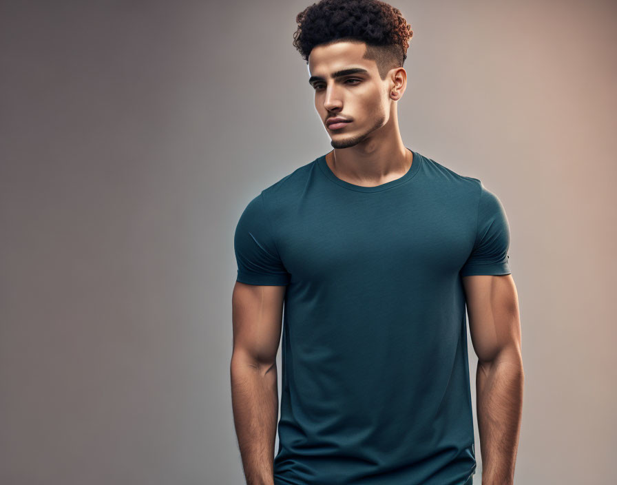 Young man with curly hair in dark teal t-shirt on neutral background