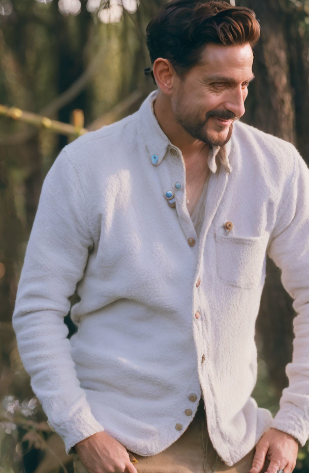 Smiling man in light cardigan outdoors with trees in background