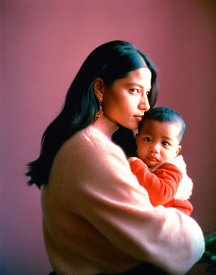 Woman in Pink Sweater Cradling Baby on Soft Pink Background