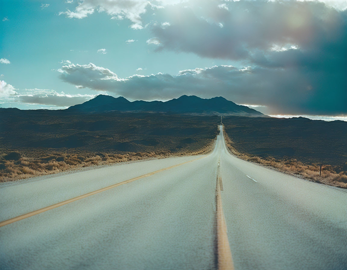 Straight Road Leading to Distant Mountains Under Dramatic Sky