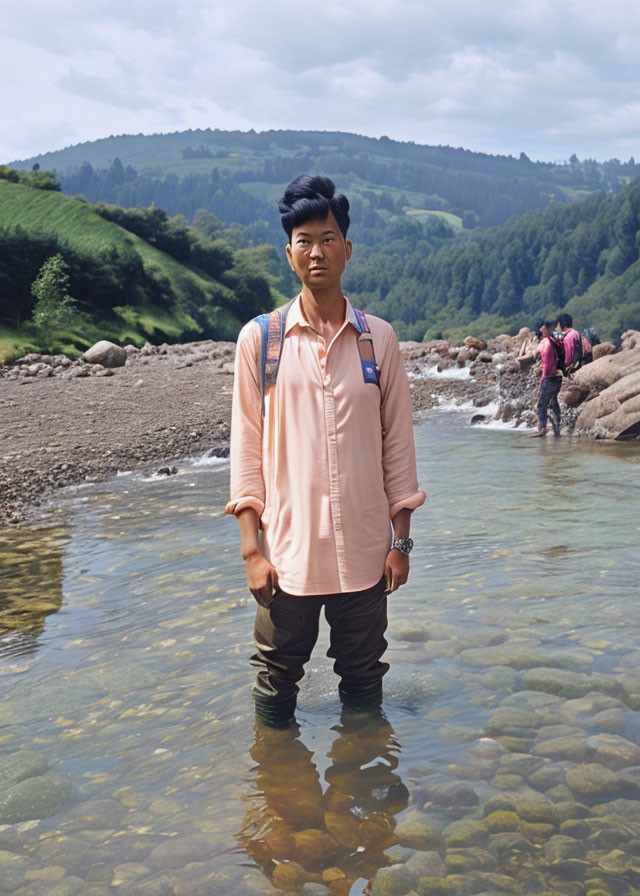 Hiker in salmon shirt and backpack in shallow river with hills - outdoor scene