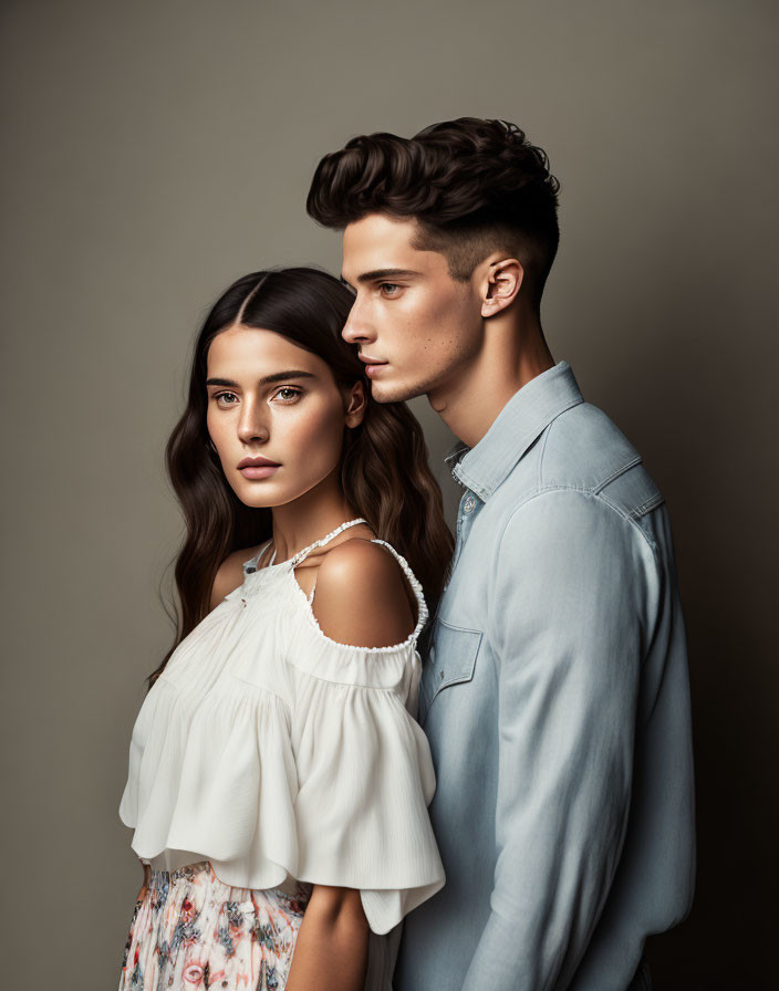 Man and woman in light blue tops posing closely on neutral background