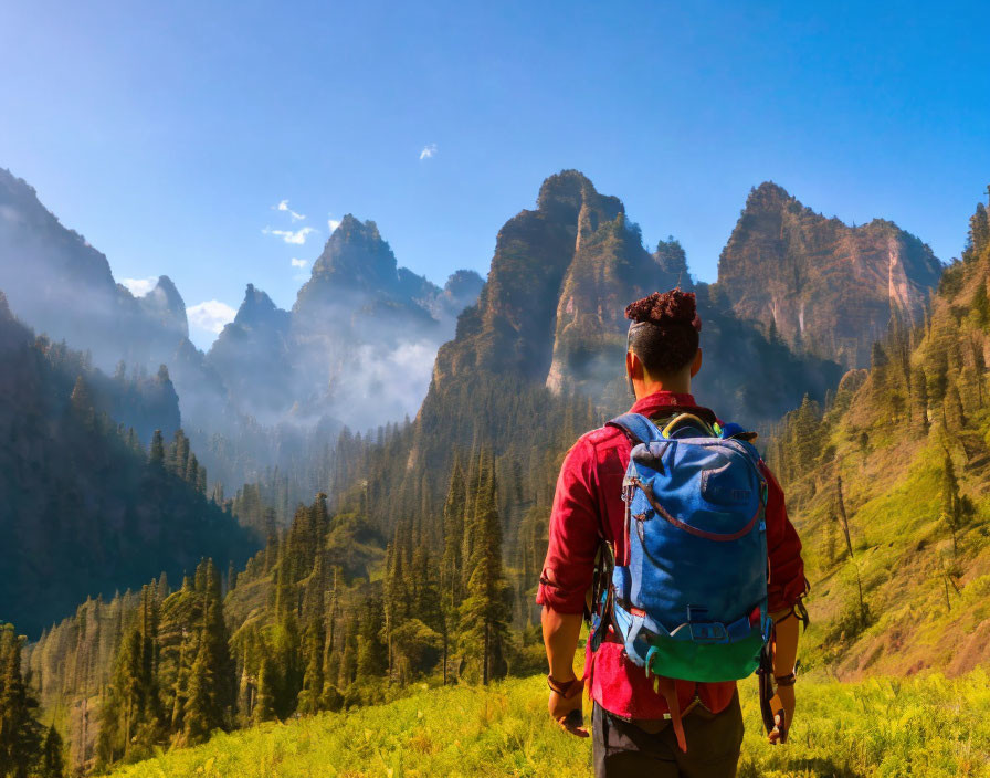 Hiker with blue backpack walking towards misty mountain peaks