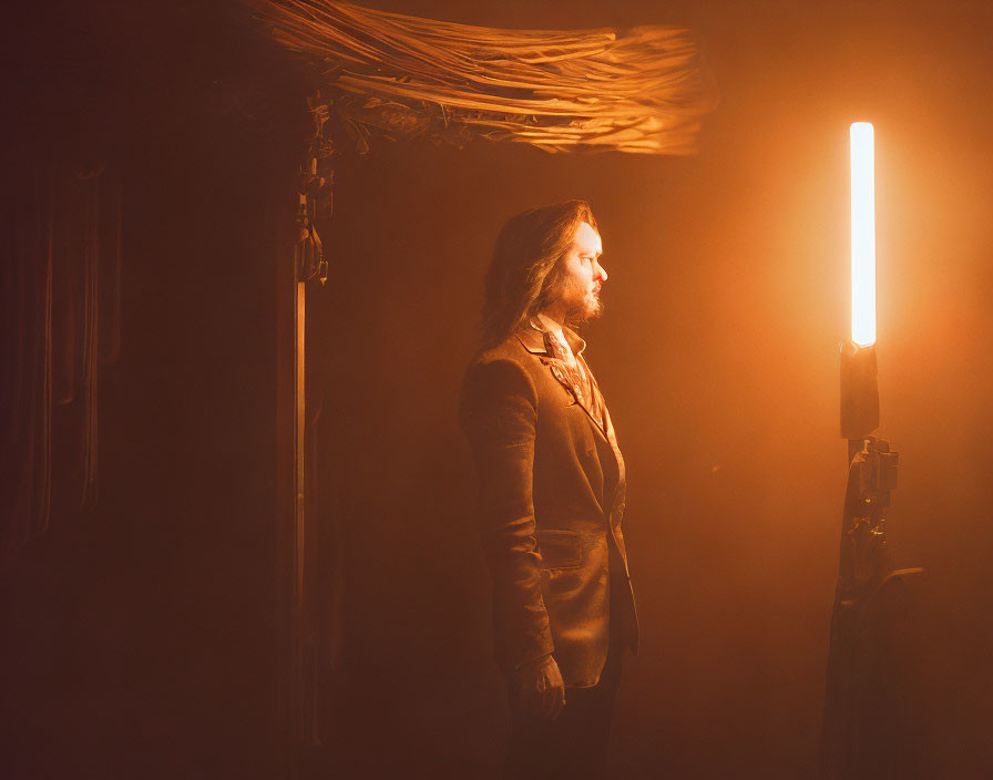 Long-Haired Man Contemplates Beside Bright Light Tube in Dim Room