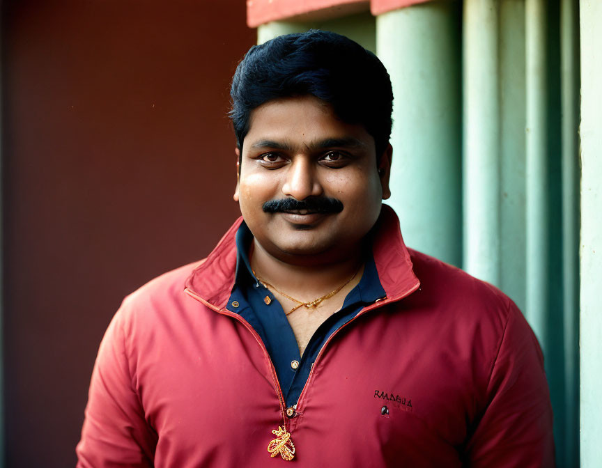 Smiling man with mustache in red and blue shirt and gold chain