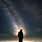 Solitary figure under starry night sky with Milky Way galaxy above.