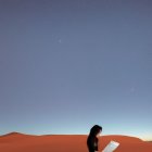 Person sitting on sand dune under starry sky at twilight