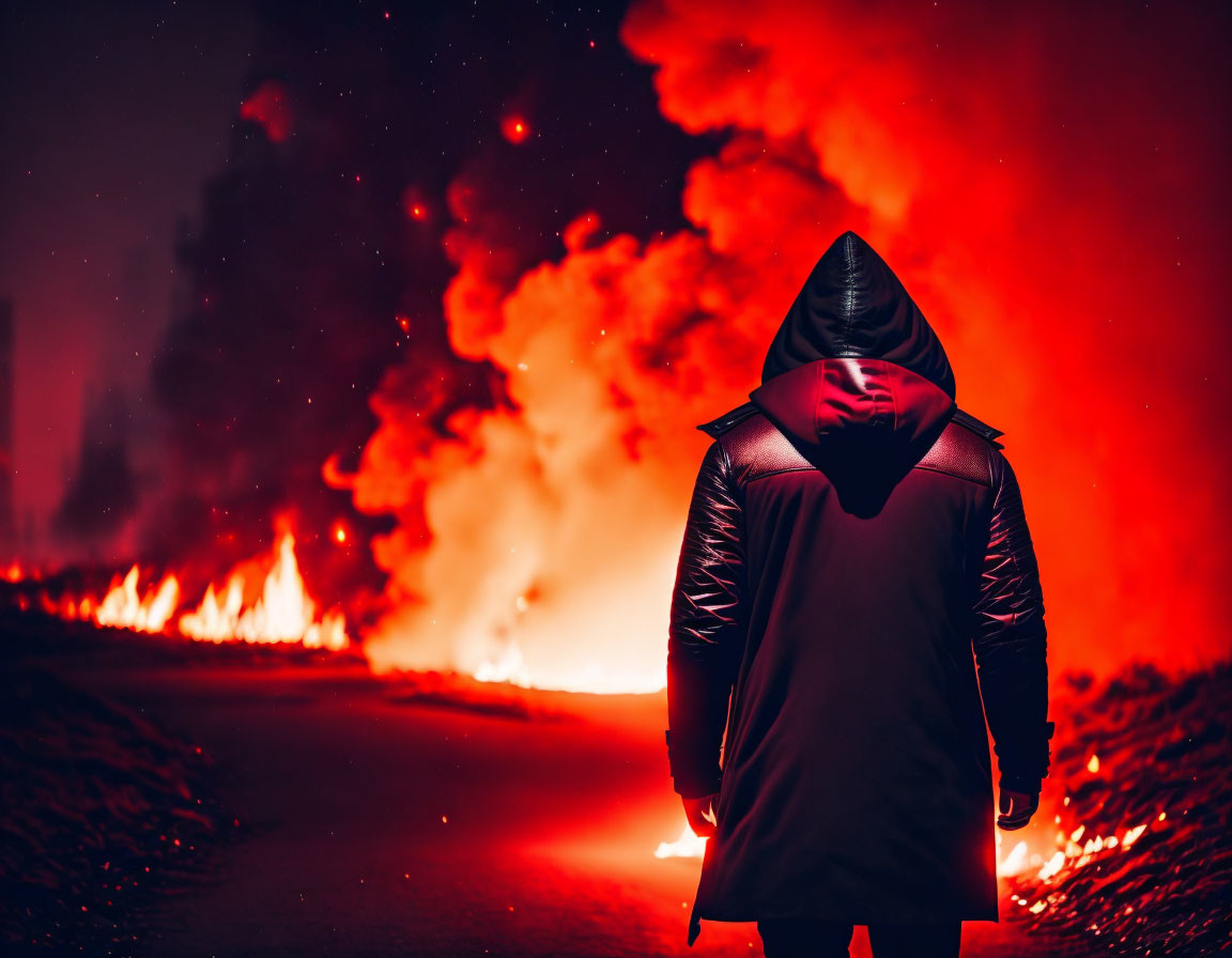 Person in hooded coat by blazing fire at night