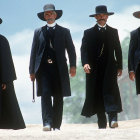 Four armed cowboys in black outfits and hats in snowy Western landscape