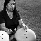 Woman interacting with large button-like sculptures on grass with scattered balls.