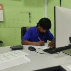 Person in Blue Shirt Works on Camera at Desk with Computer and Accessories