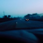 Vehicle headlights illuminate misty twilight road through blurry windshield