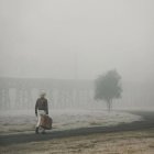 Person in hat walking on foggy path with distant figure