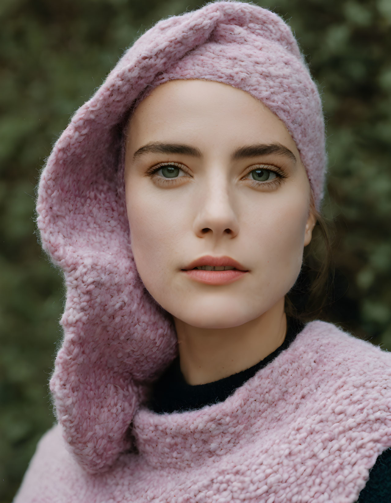 Fair-skinned woman in pink headscarf and black top on blurred green backdrop