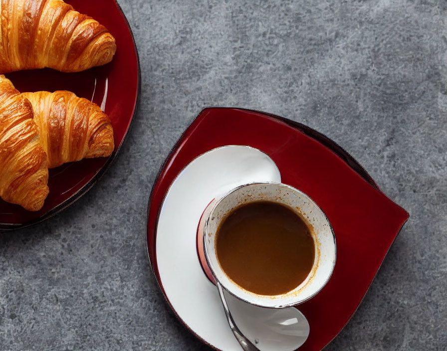 Coffee and croissants on red plate with saucer on gray surface