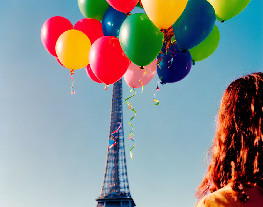 Person holding colorful balloons with Eiffel Tower backdrop on clear day