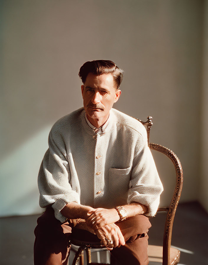 Man with Mustache in Light Sweater and Brown Trousers Sitting on Chair