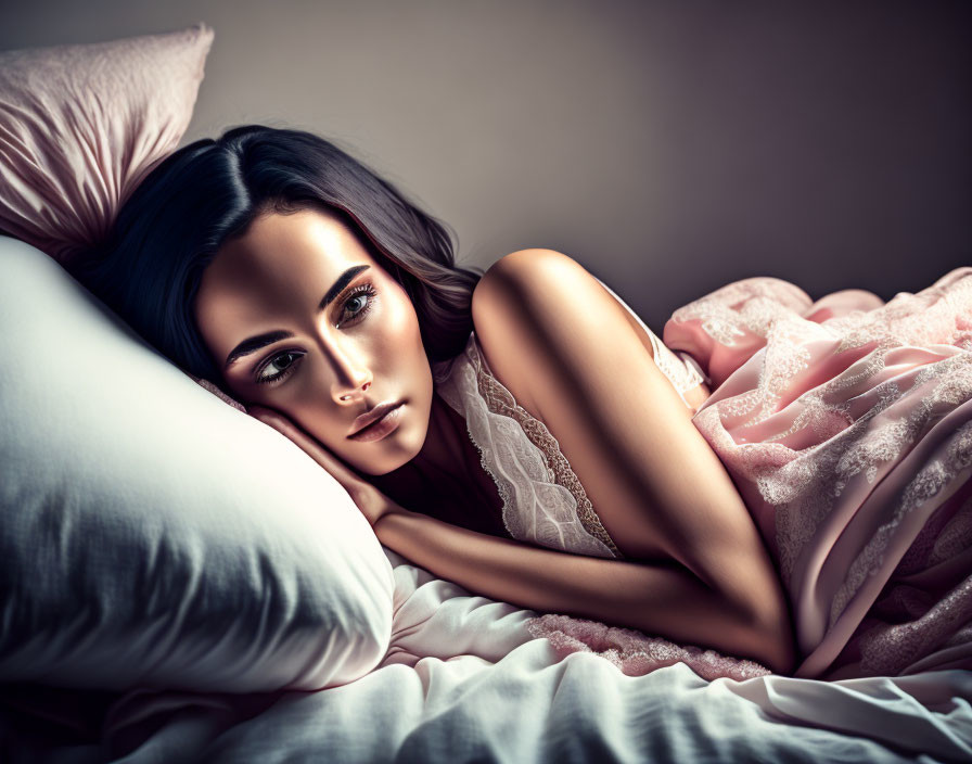 Woman lying on bed in pink lace garment with introspective gaze