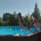 Kids playing in backyard pool with greenery and birds in clear sky