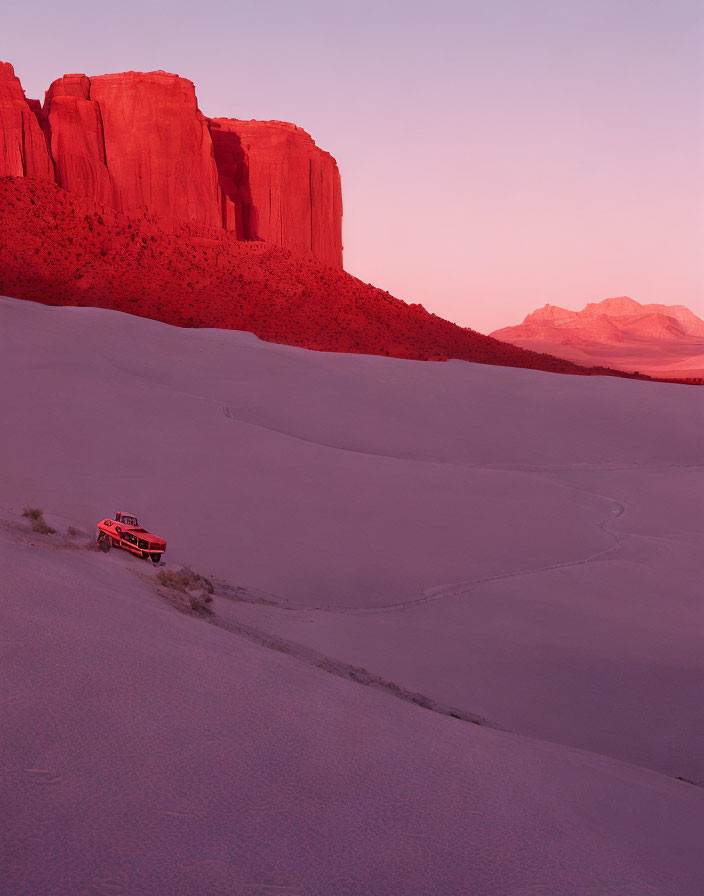 Red Vehicle Descending Sand Dune with Track Marks, Red Cliffs, Pink Dusk Sky