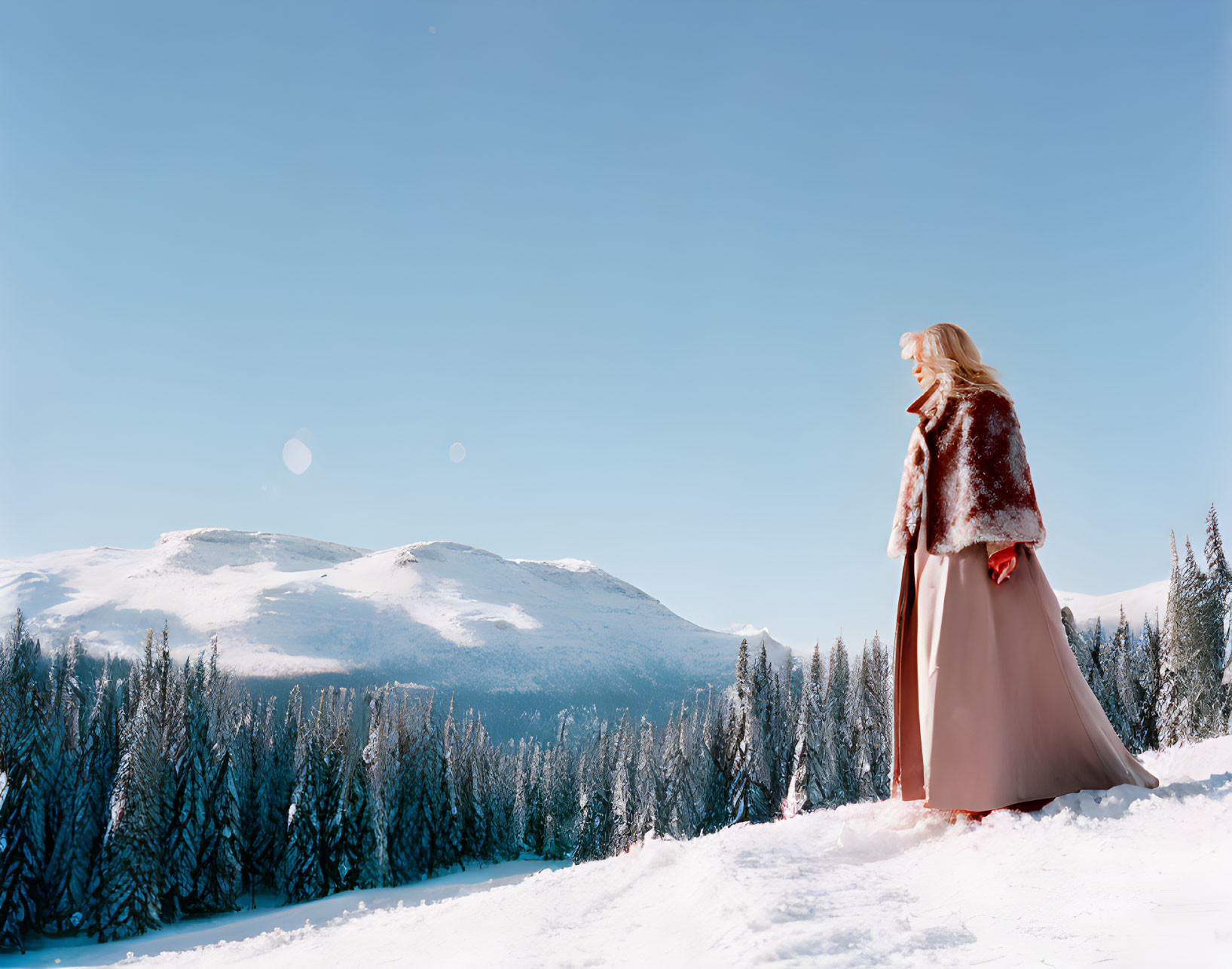 Woman in Red Cloak in Snowy Landscape with Pine Trees and Mountains