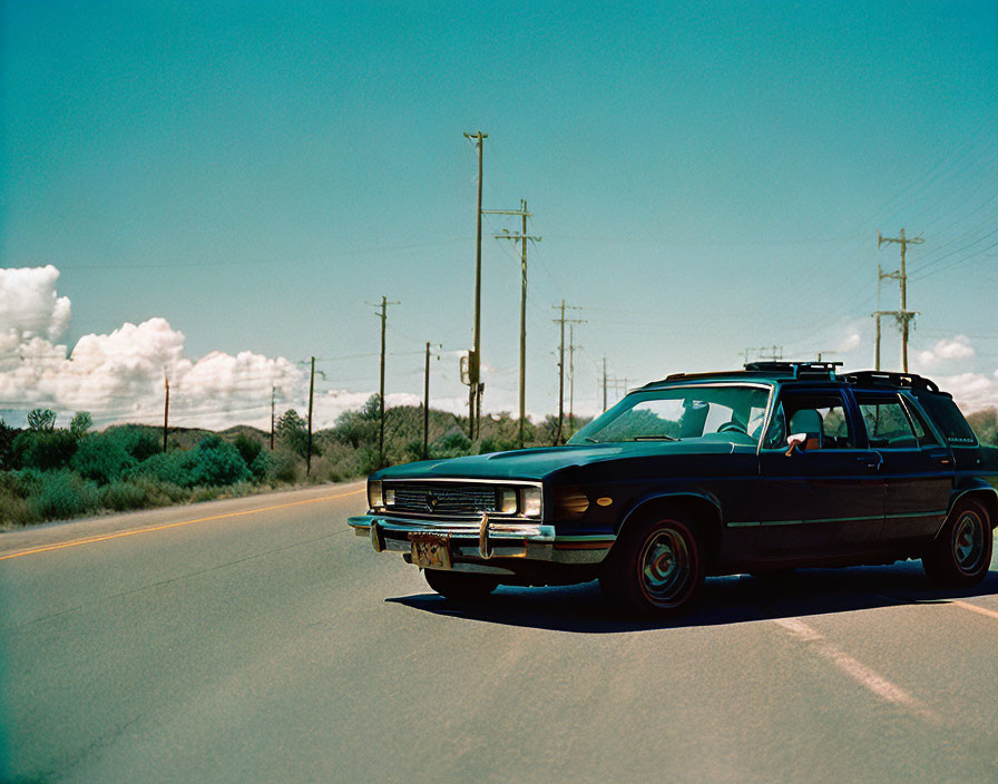 Vintage station wagon on sunny road with telephone poles & fluffy clouds