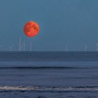 Scenic windmills by water at dusk with red moon & stars