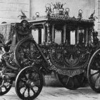 Black and Gold Carriage with Elaborate Horse Sculptures and White Detailed Interior