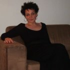 Woman with updo hairstyle in black dress sitting on brown couch.