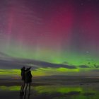 Aurora display with green and pink colors over calm water