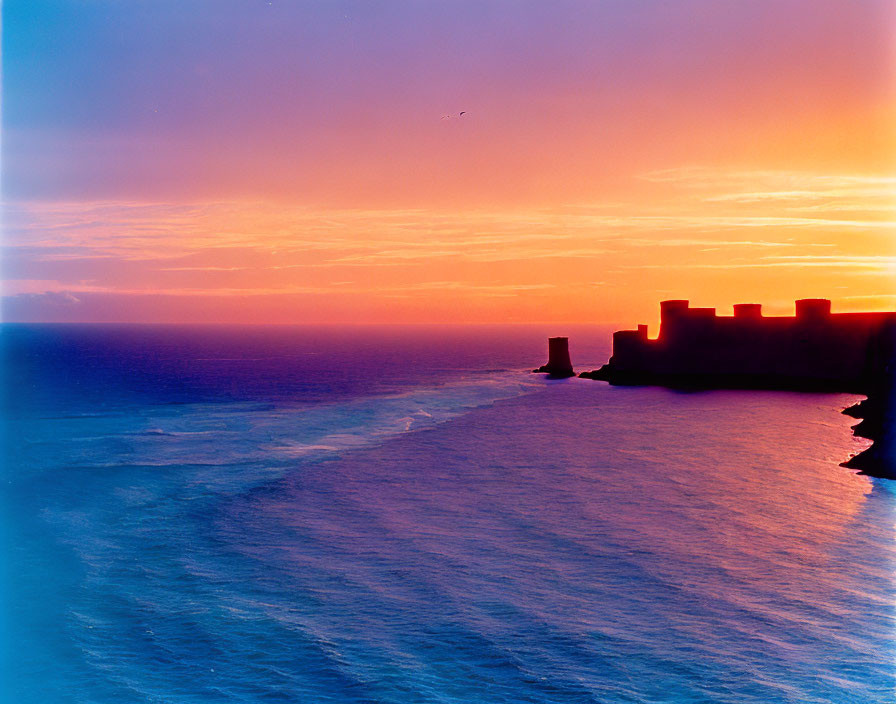 Scenic sunset over ocean with fortress silhouette and calm sea.