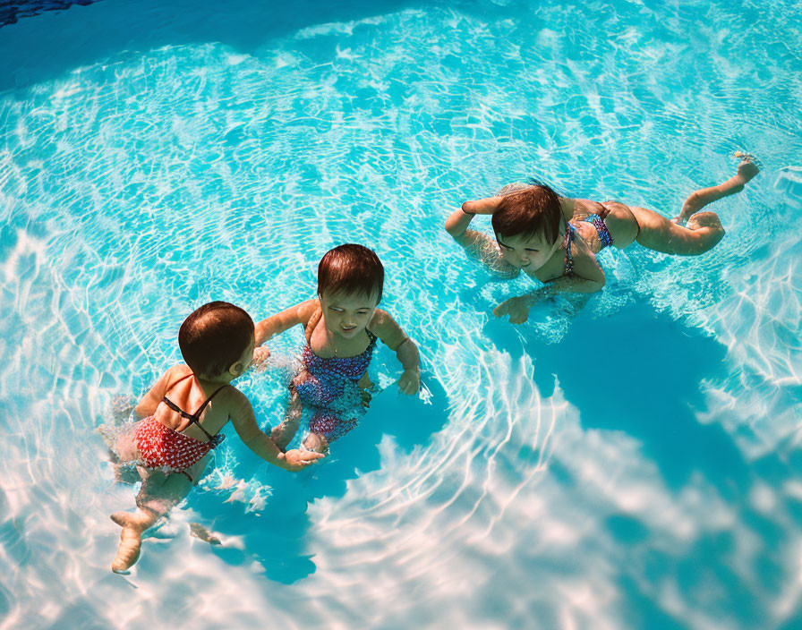 Children playing in clear blue pool under sunlight shadows