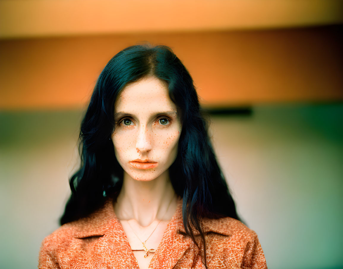 Woman with Dark Hair and Freckles in Orange Top on Warm Background