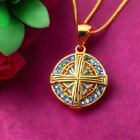 Gold cross pendant with blue gemstones on pink surface next to red rose