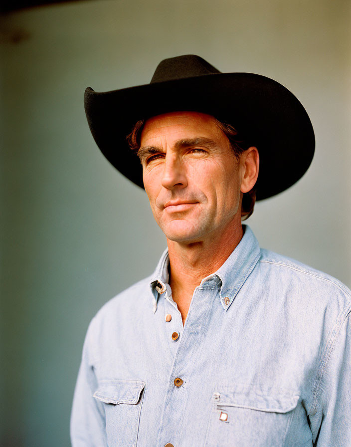 Man in Black Cowboy Hat and Denim Shirt Against Blurred Background