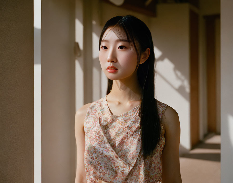 Woman in Floral Dress Standing by Open Door in Sunlit Corridor