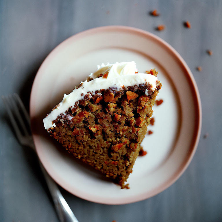 Carrot cake slice with cream cheese frosting on pink plate, gray background