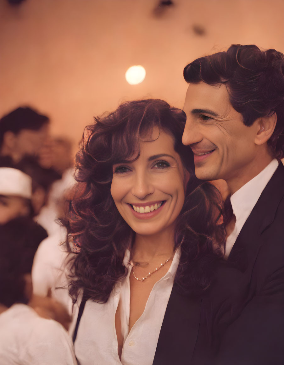 Smiling woman with curly hair embraced by man in suit in warm-toned setting