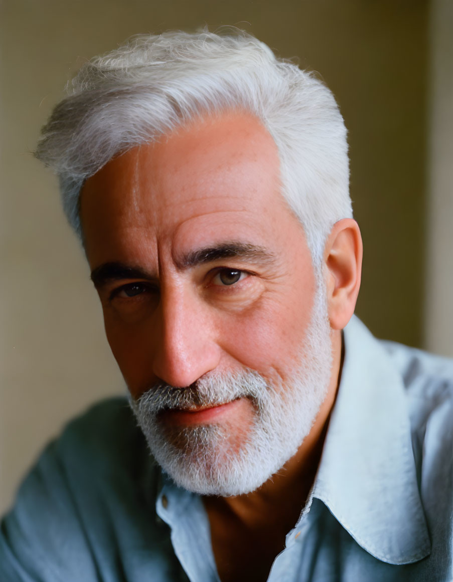 Smiling man with white hair and beard in light blue shirt